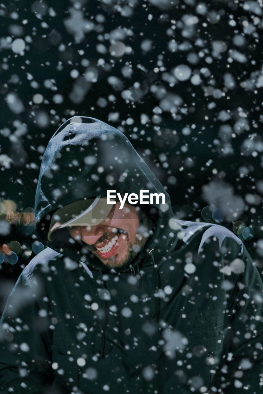 Happy man wearing warm clothing while standing during snowfall at night