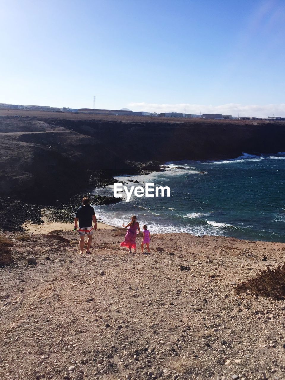 REAR VIEW OF FRIENDS WALKING ON BEACH AGAINST SKY