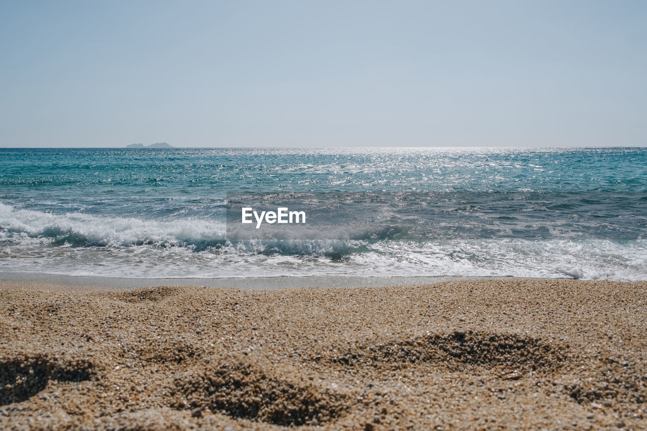 View over the sand of waves washing up on a beach on a sunny summer day, focus on background .