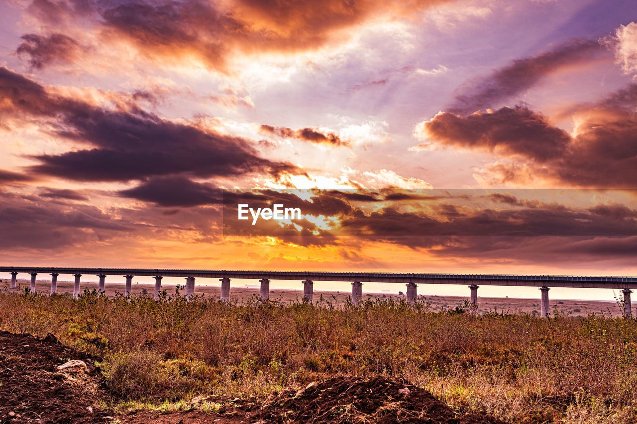 sky, cloud, sunset, water, horizon, nature, sea, land, beauty in nature, scenics - nature, beach, dusk, landscape, environment, evening, tranquility, sunlight, coast, dramatic sky, tranquil scene, no people, shore, afterglow, horizon over water, outdoors, architecture, travel destinations, idyllic, sun, orange color, travel, seascape, ocean, grass, cloudscape, plant, silhouette, non-urban scene, built structure, tourism, bridge