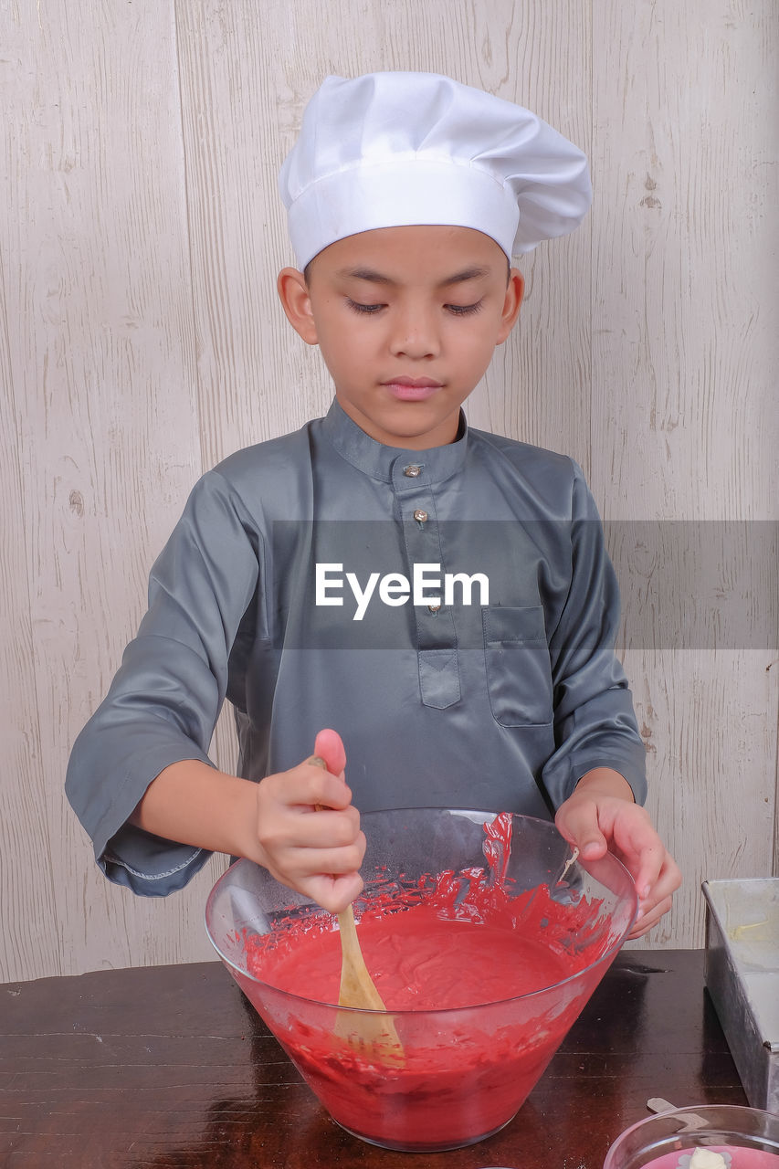 Boy mixing batter in bowl on table at home