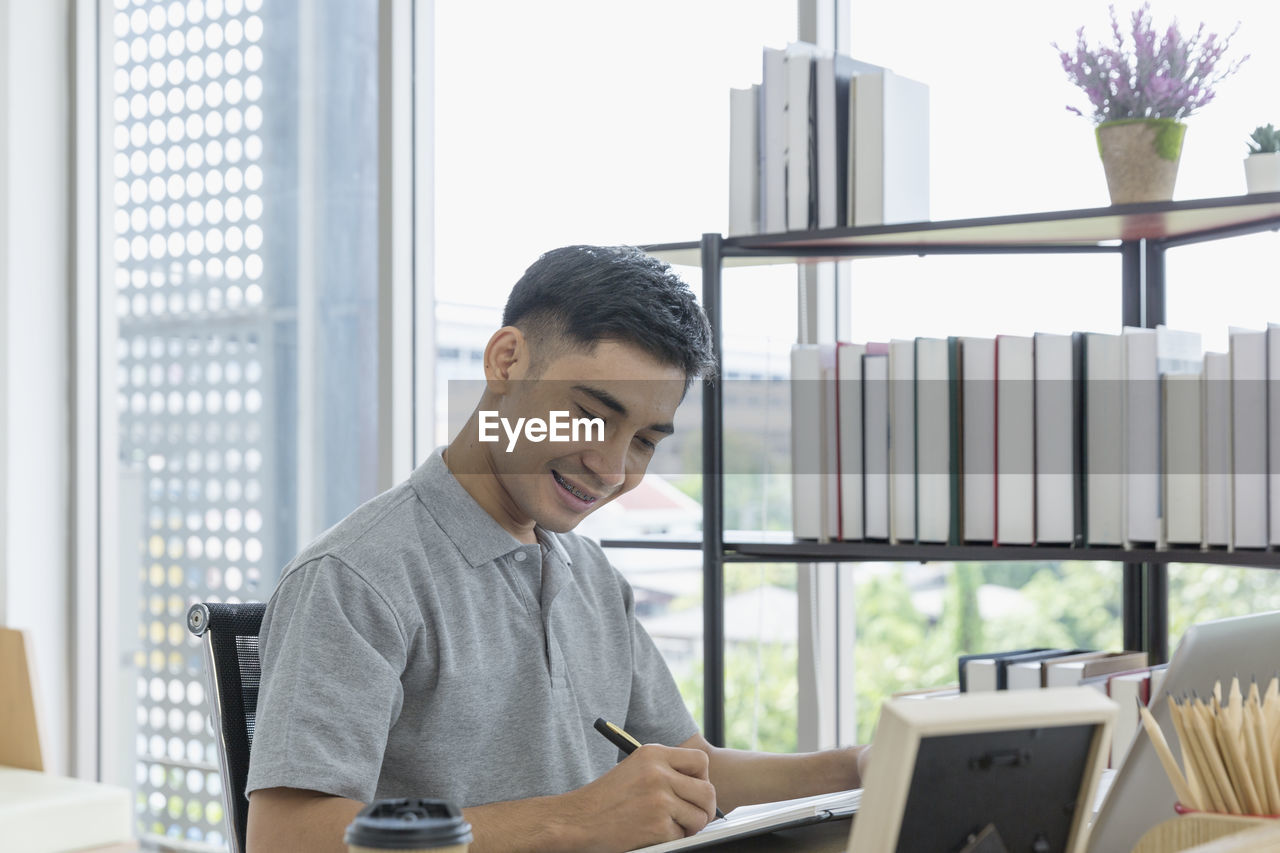 MAN LOOKING AT CAMERA WHILE SITTING IN LAPTOP