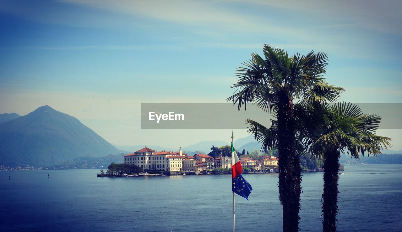 Palm trees and italian and european - eu - flags by sea against sky with island in the background