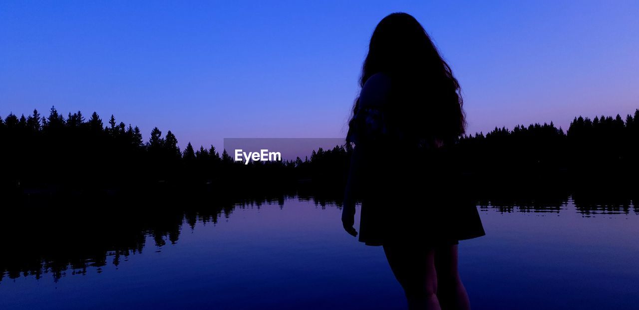 Silhouette woman standing by lake against sky during sunset