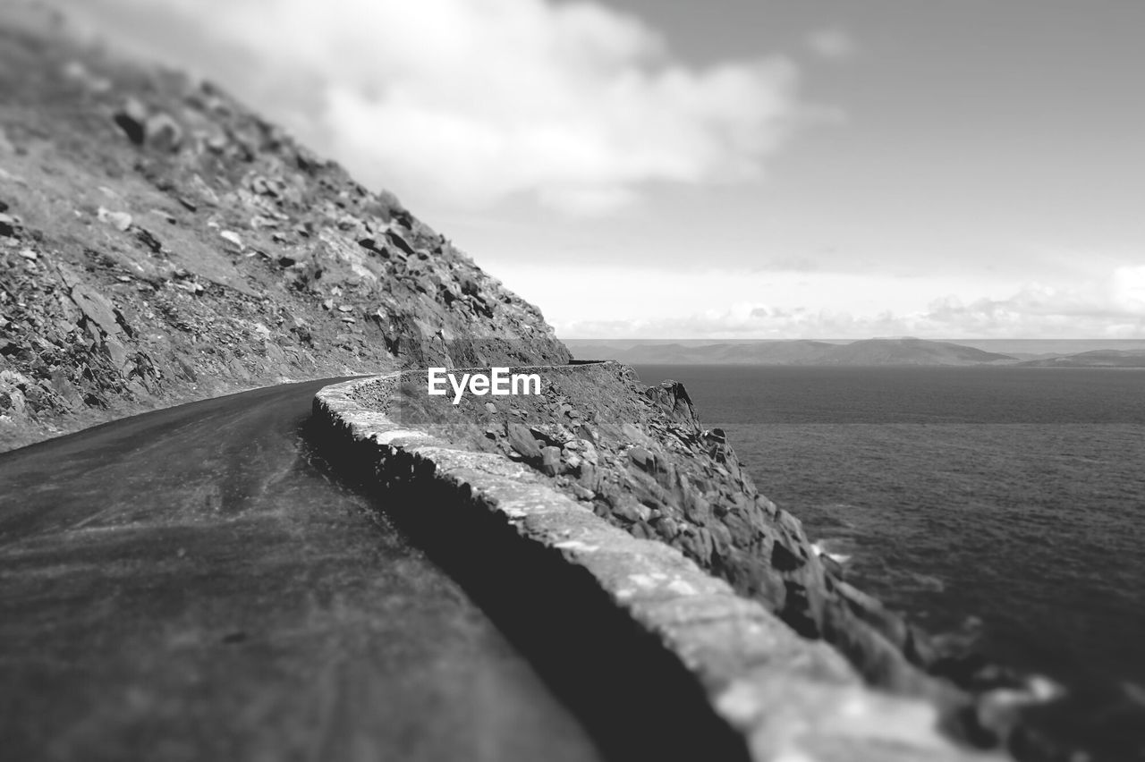 Mountain road by sea against cloudy sky