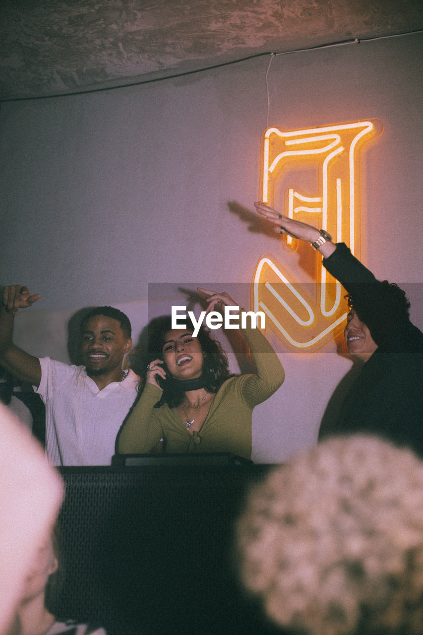 Happy young female dj amidst friends enjoying at nightclub