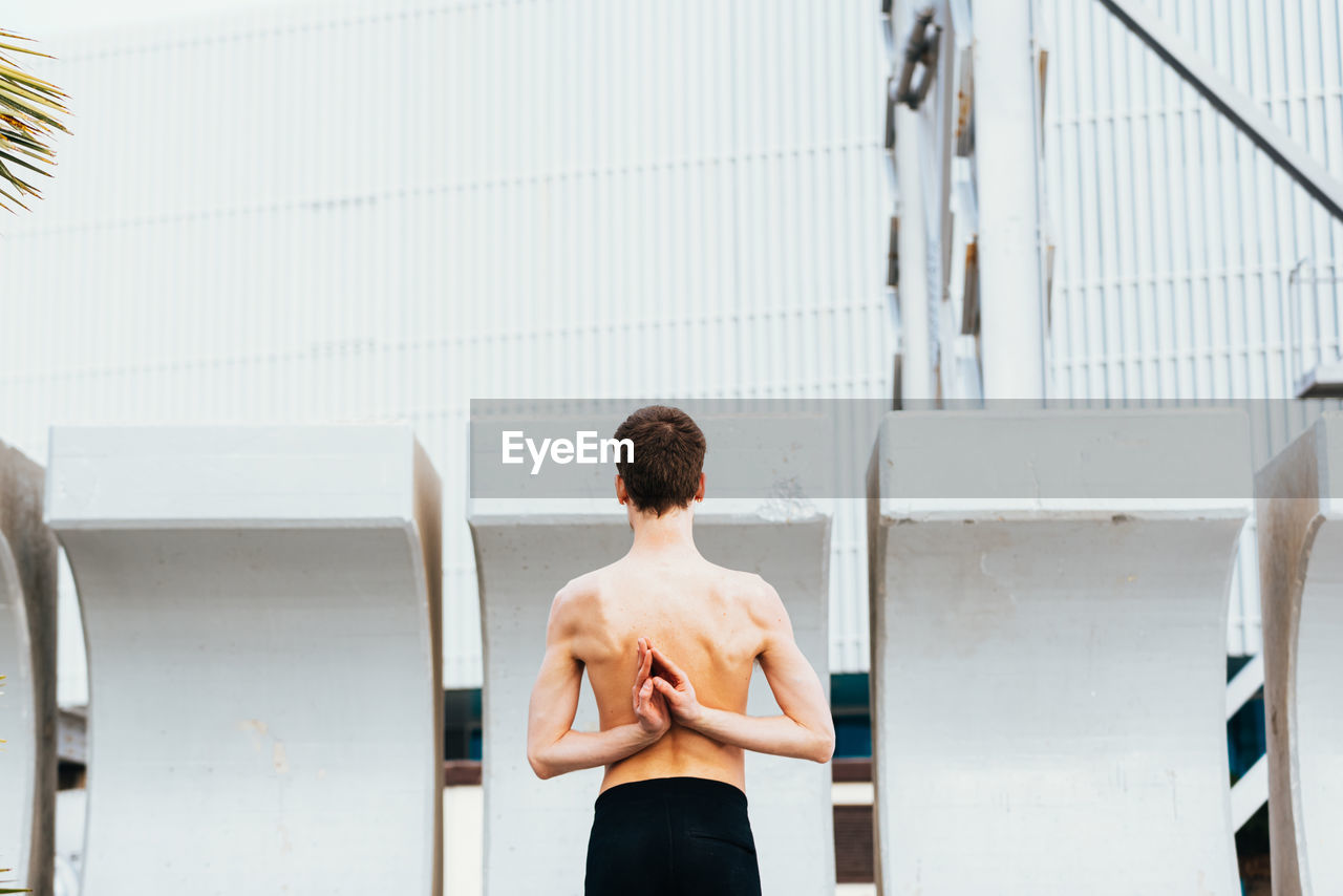 Rear view of shirtless man standing against wall