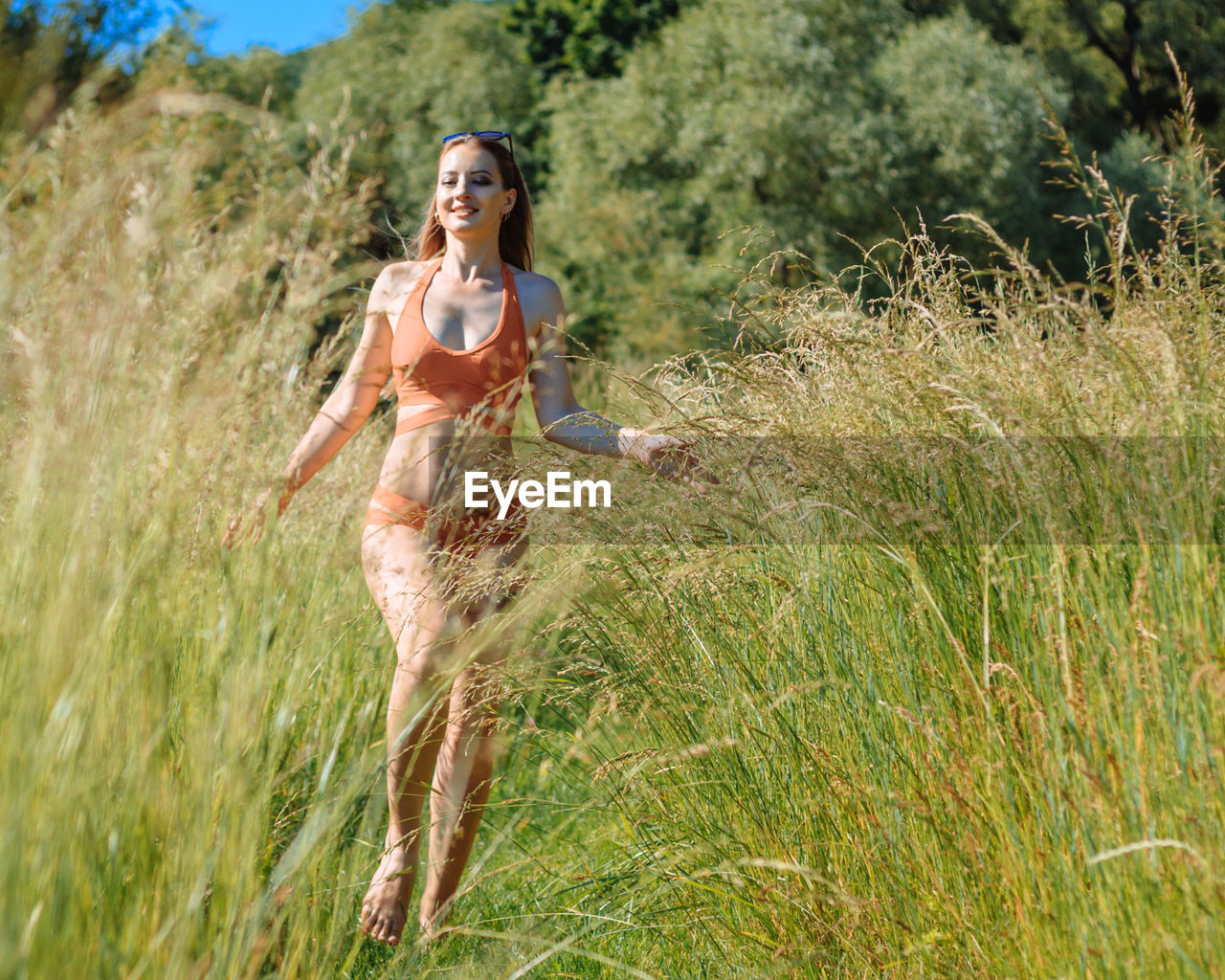 Sexy slender blonde girl in a red bikini runs around the field among the tall grass on a summer day