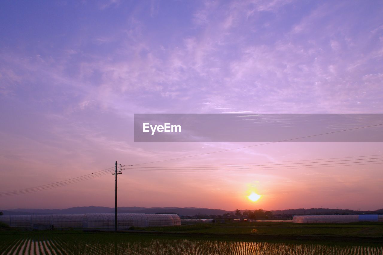 Electricity pylon on landscape against romantic sky at sunset