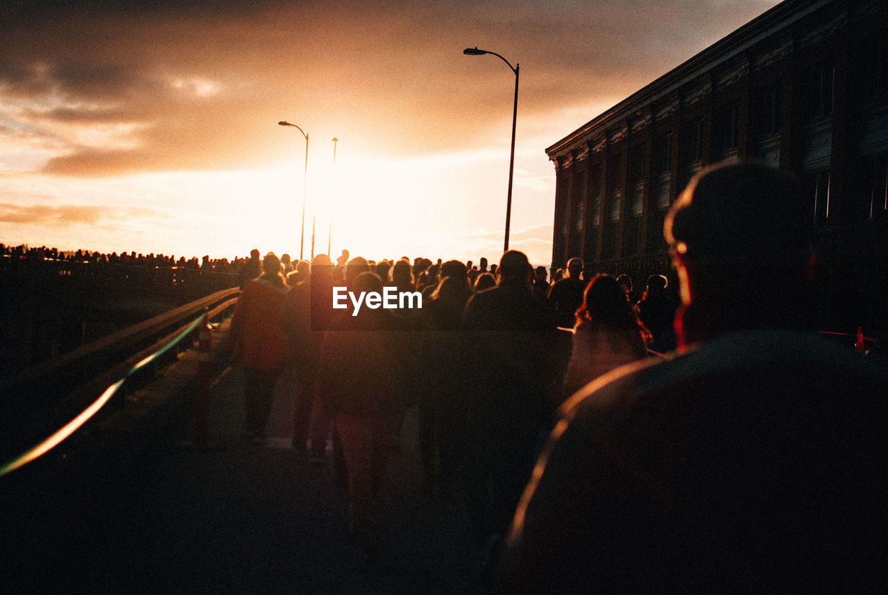 People on street in city against sky during sunset