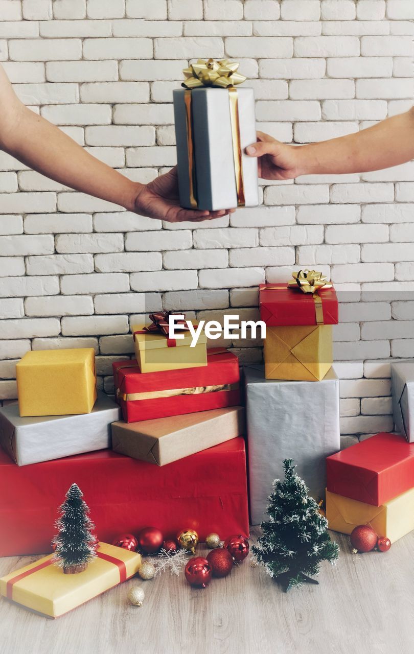 Cropped hands of people holding gift against wall at home