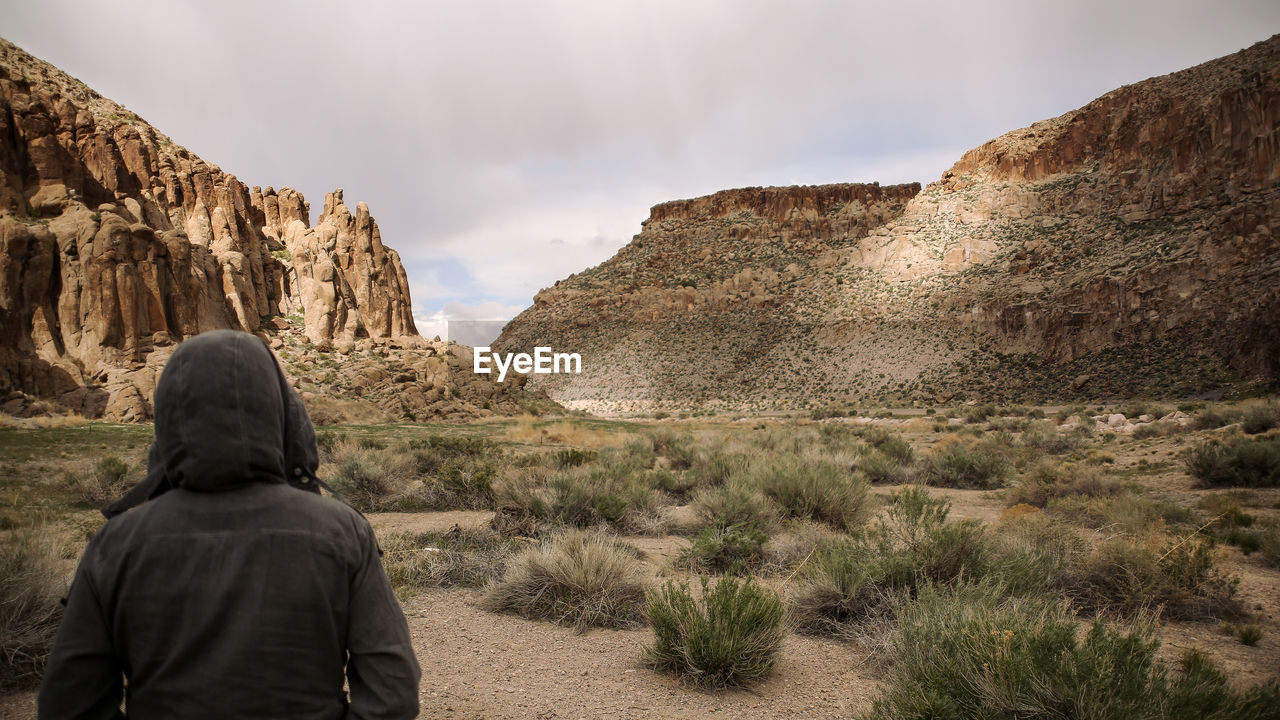 Rear view of hooded person by rocky mountains against sky