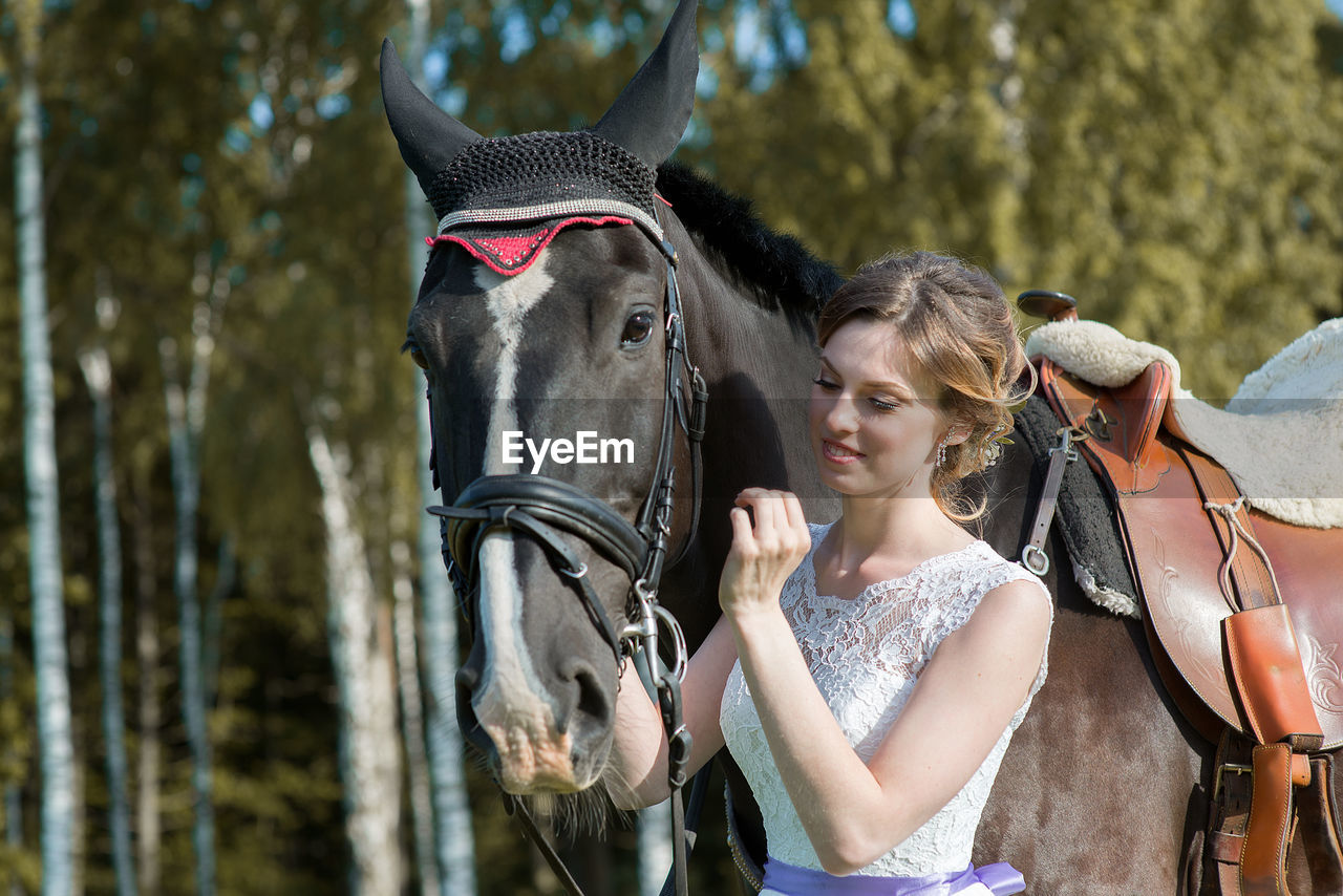 Young woman standing by horse on field during sunny day