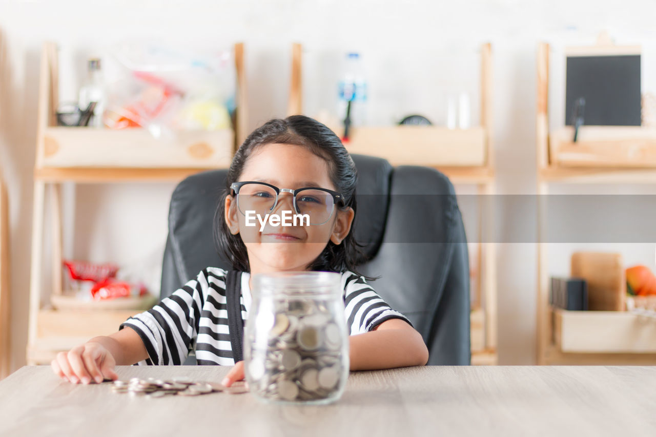 Portrait of girl sitting by coins at home