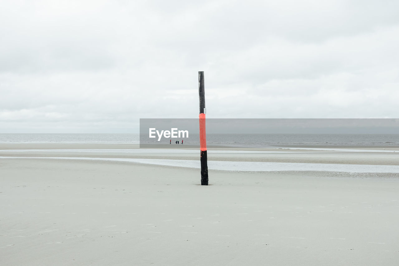 MAN STANDING ON BEACH AGAINST SKY