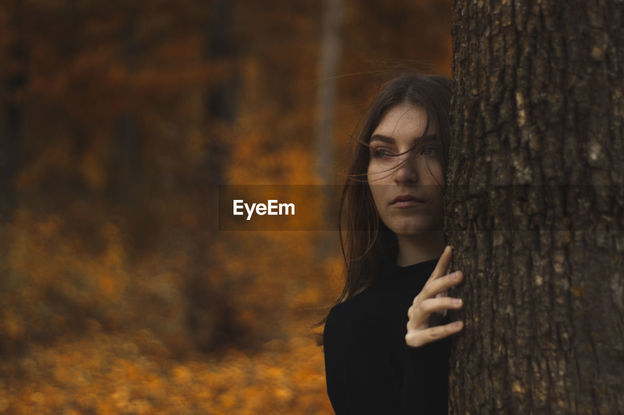 Beautiful woman standing by tree trunk in forest