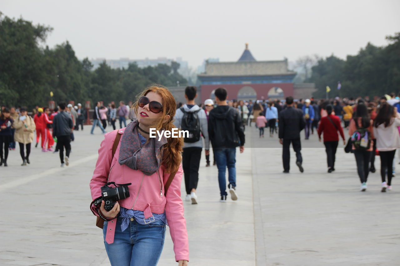 Beautiful woman with digital camera standing on street in city