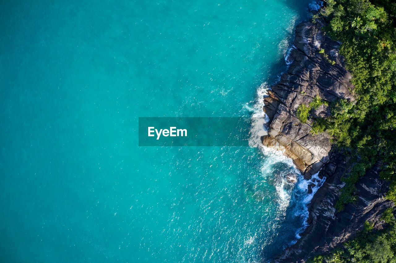 Drone field of view of secret cove with turquoise water meeting the forest of mahe, seychelles.
