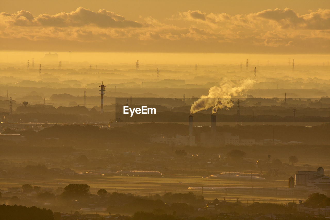 Aerial view of smoke emitting from factory against cloudy sky during sunset