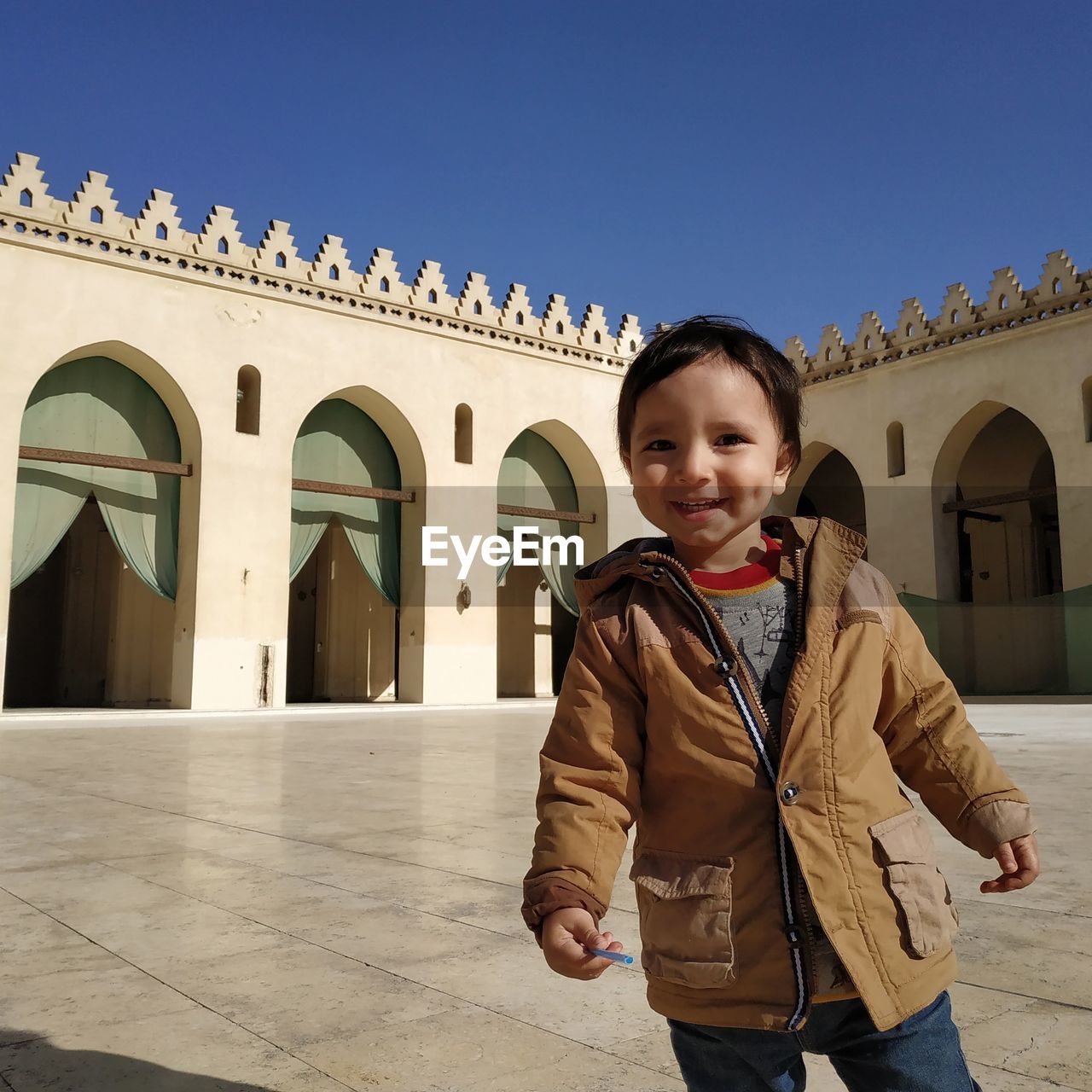 Portrait of smiling cute boy standing on footpath against mosque