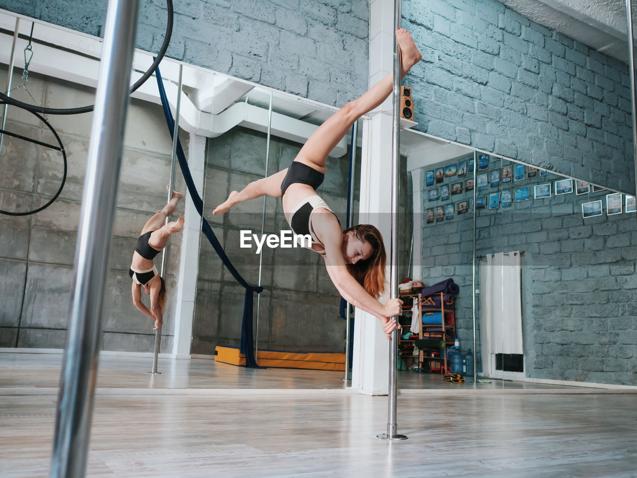 Sensuous woman practicing pole dance reflecting on mirror in studio