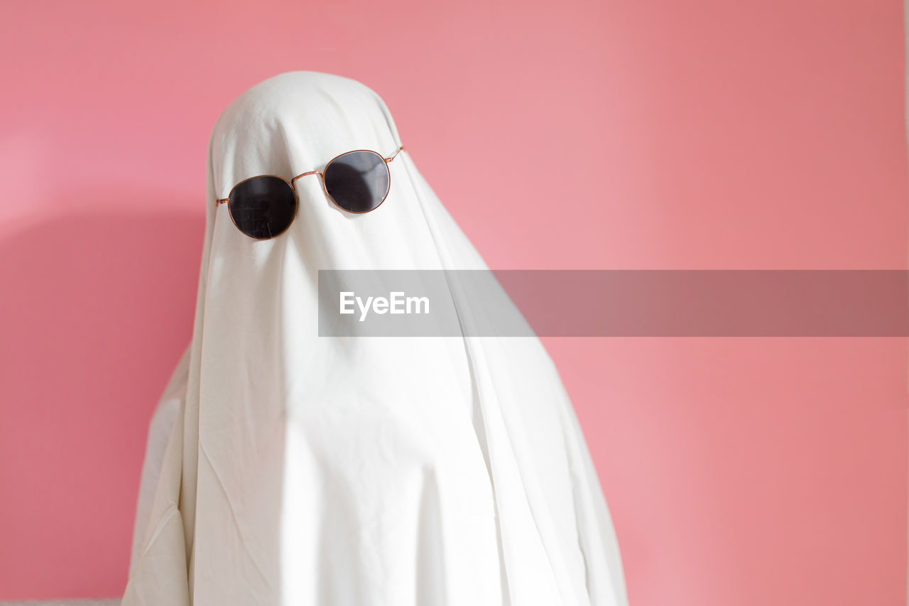 Cute sheet ghost costume with sunglasses on a pink background. halloween party carnival concept.