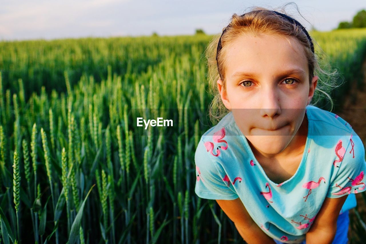 Portrait of girl bending against crops at farm