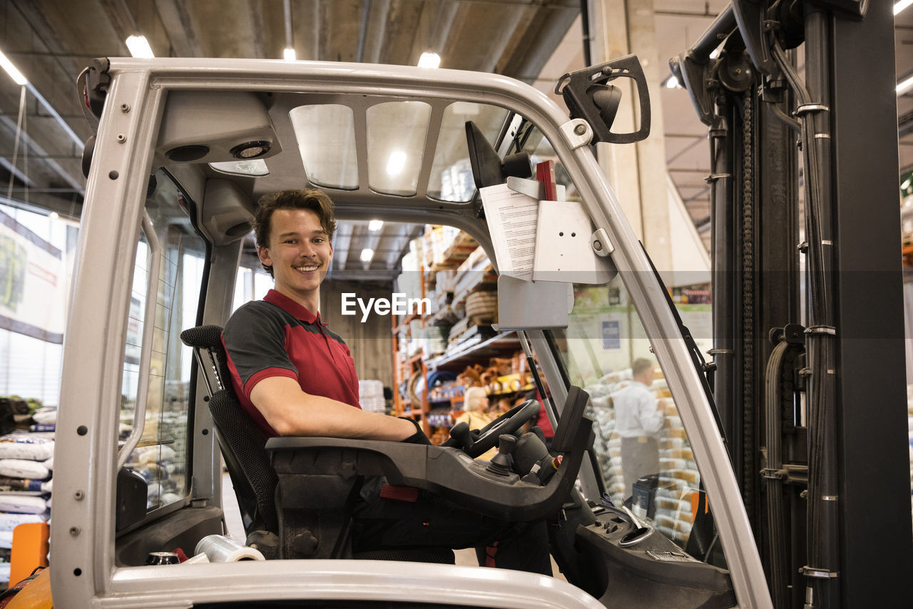 Smiling warehouse worker sitting in forklift at warehouse