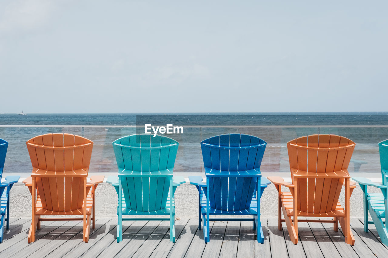 Empty chairs at beach against sky