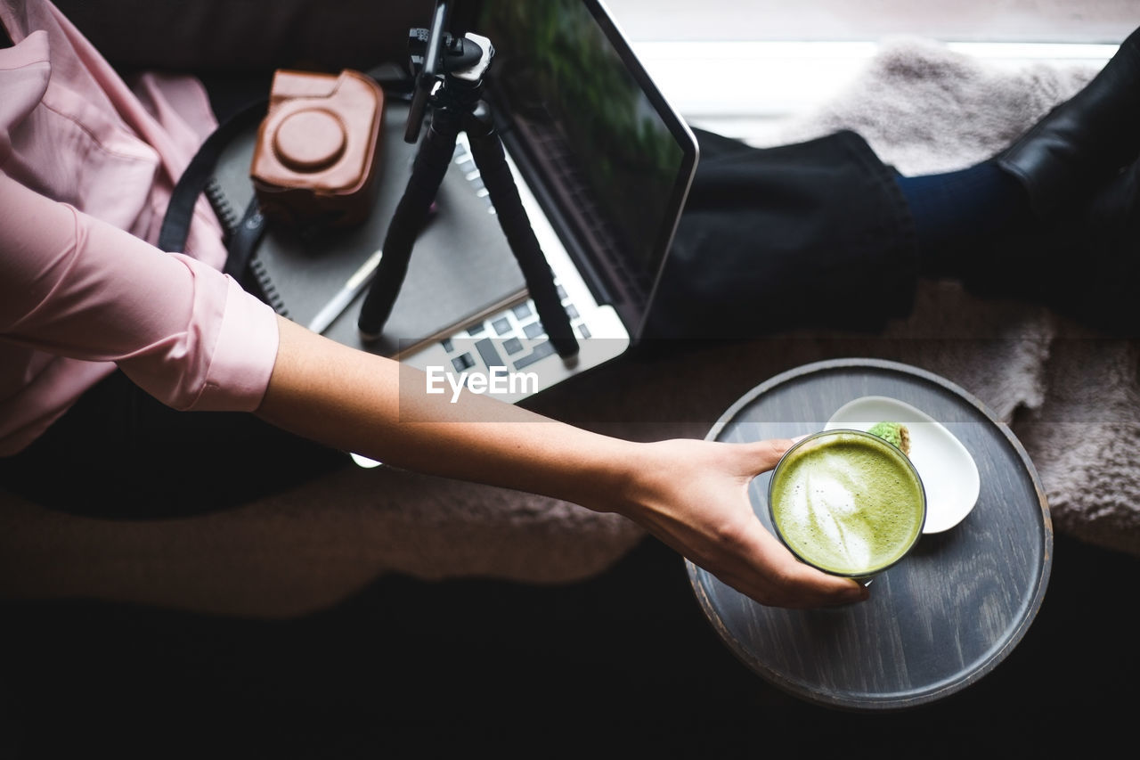 High angle view of young female influencer drinking matcha tea while making vlog at creative office