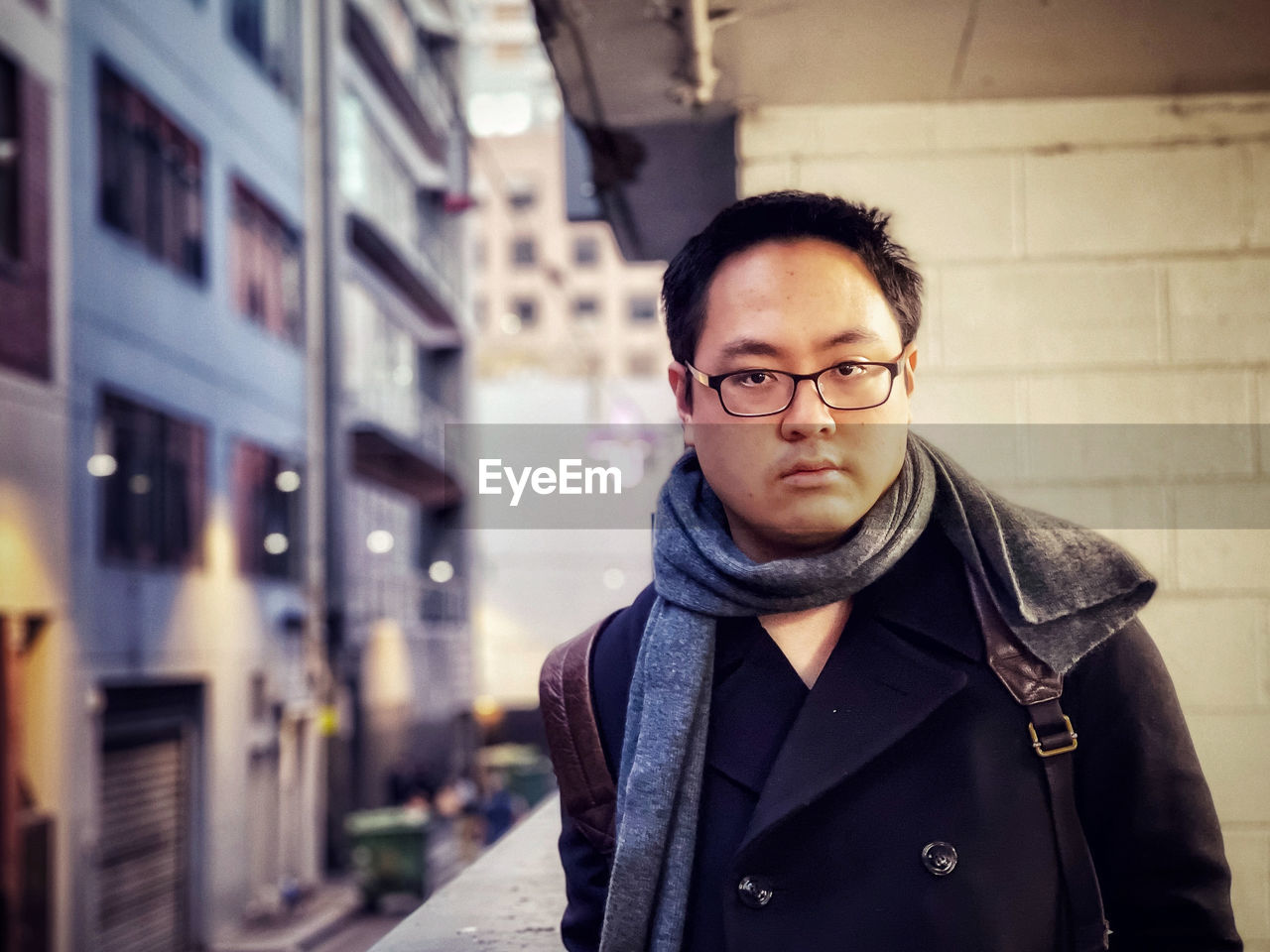 Portrait of young man standing against wall and building exteriors in city lane way.