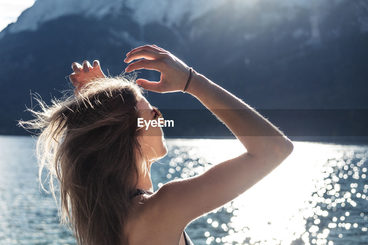 Woman with arms raised looking at view at eibsee lake during sunny day