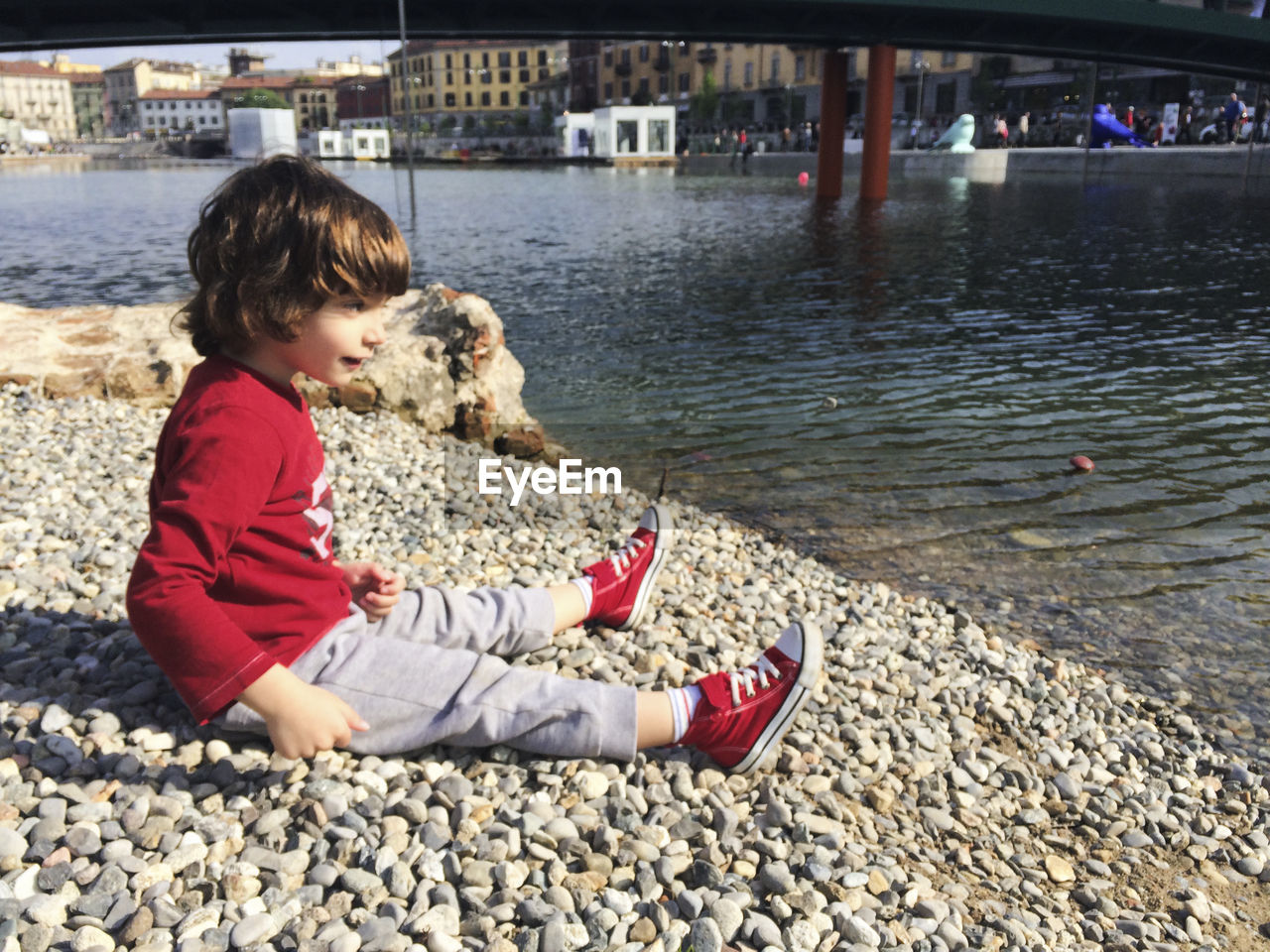 Cute boy sitting at lakeshore in city