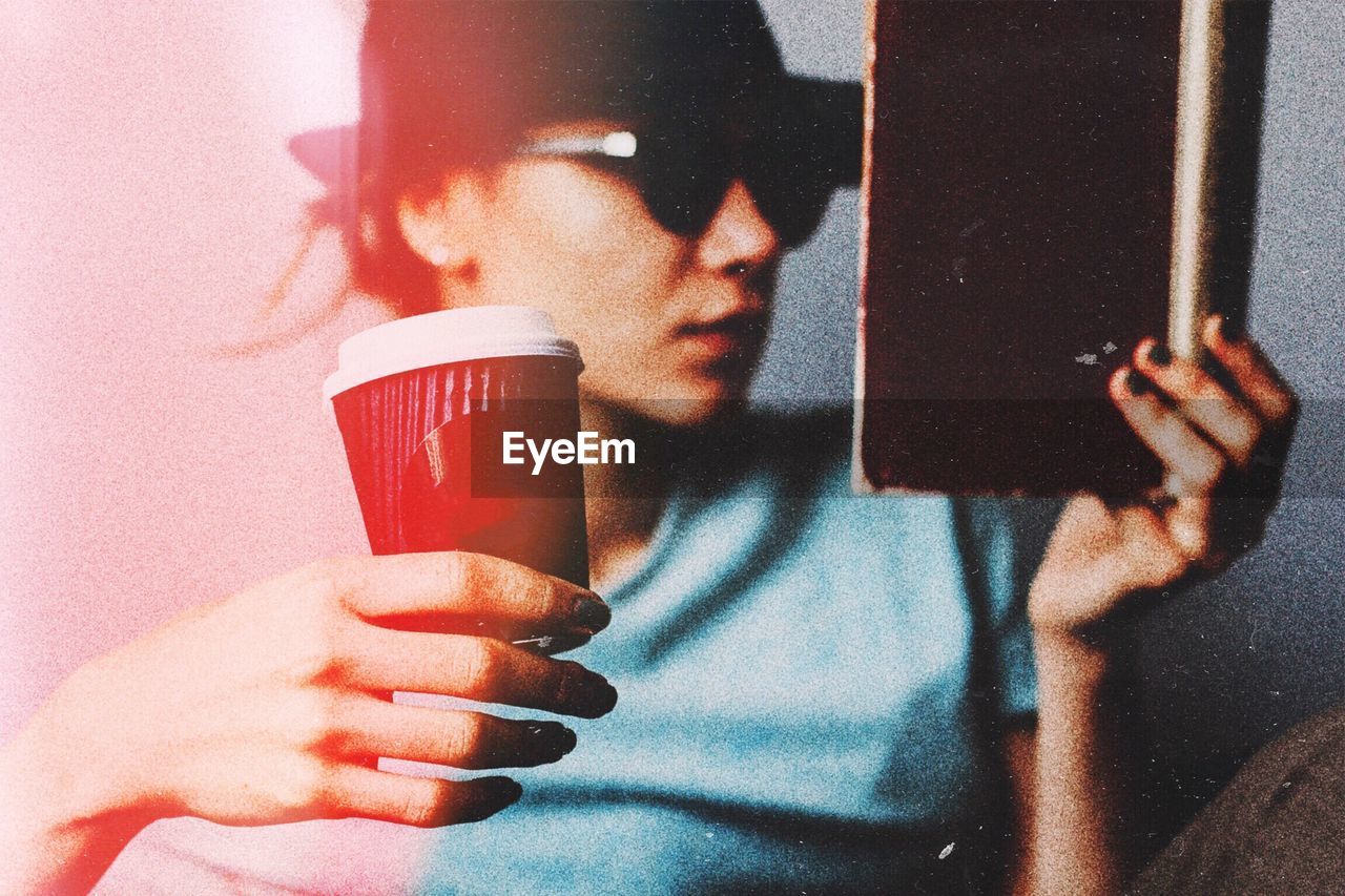 Close-up of woman holding coffee while reading book