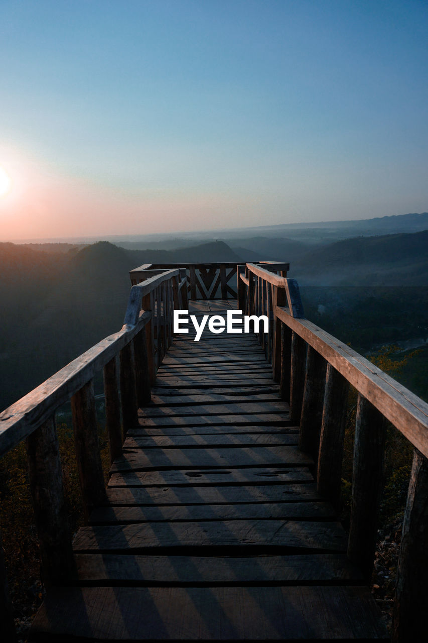 Empty long wooden footbridge against clear sky