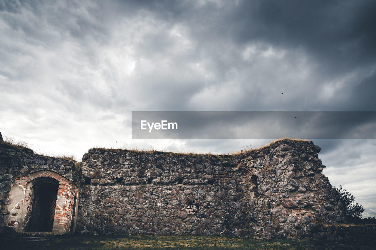 Low angle view of abandoned castle against cloudy sky