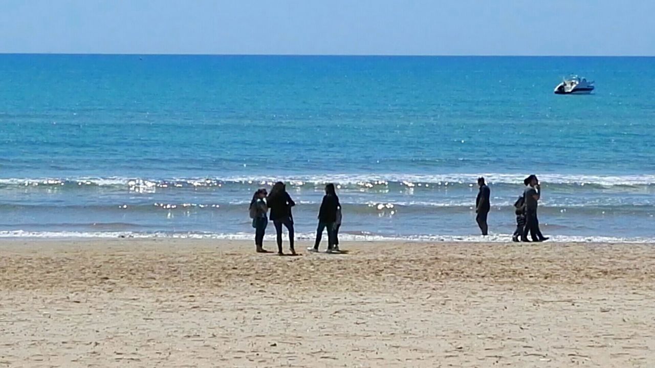 PEOPLE ON BEACH AGAINST SEA