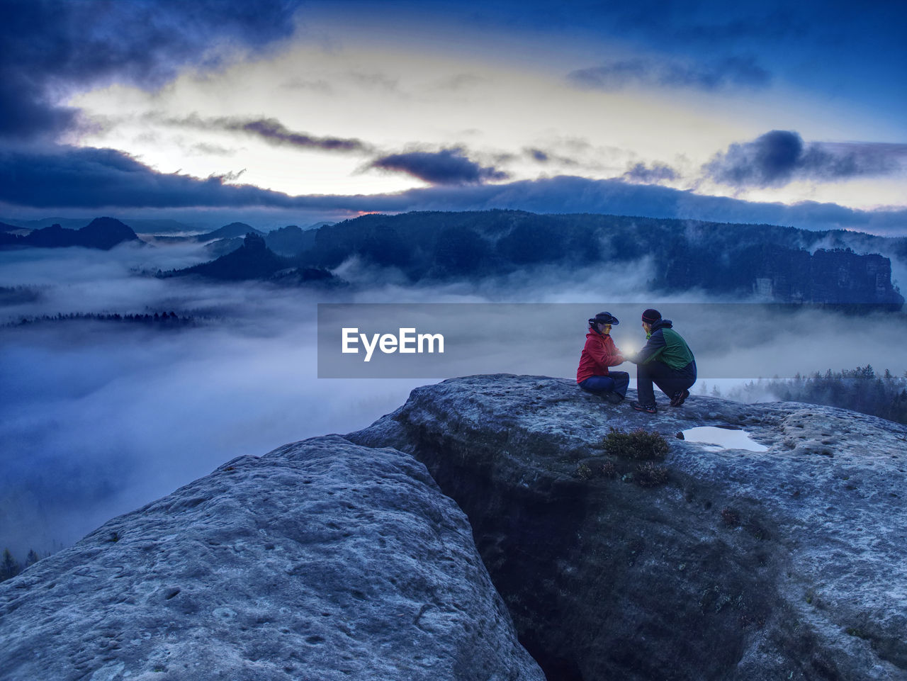 Couple hold light high above danger gulch between rocks. night mountains. lovers standing on peak