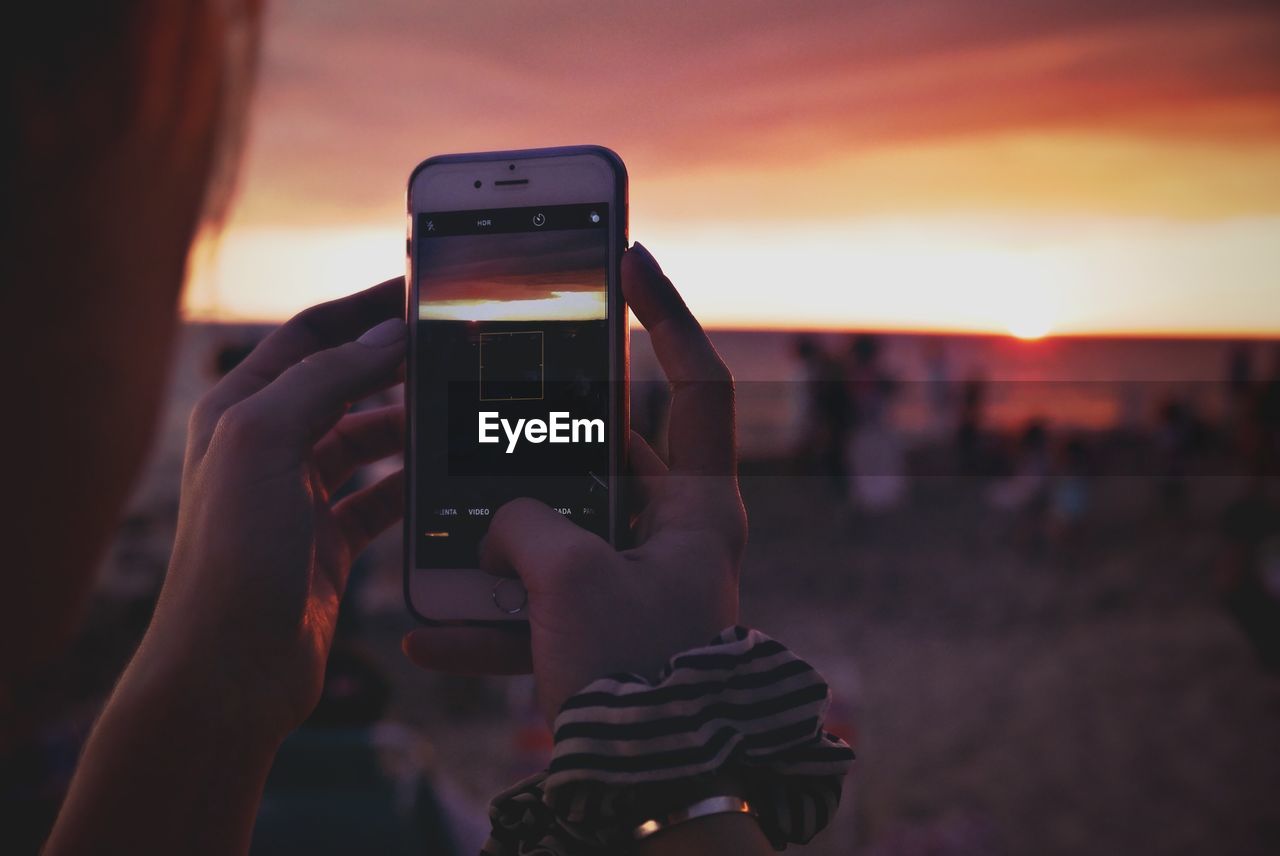 Cropped hand photographing sunset