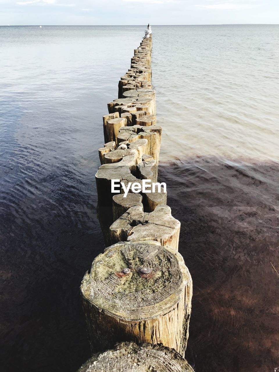 STACK OF ROCKS ON WOODEN POST BY SEA AGAINST SKY