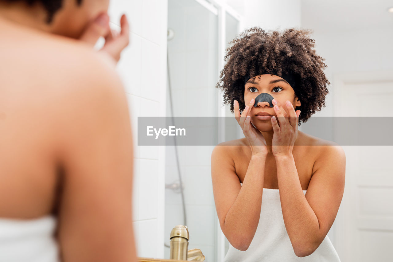 Reflection of woman applying facial mask in mirror at home