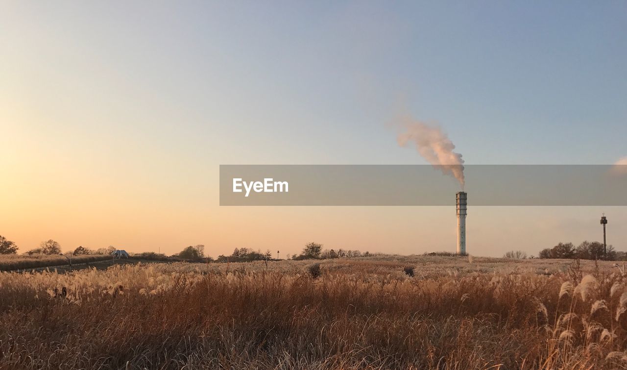 Smoke emitting from chimney on field against sky