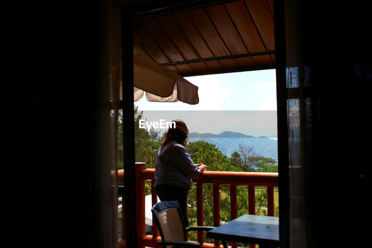 Woman standing in balcony seen through window