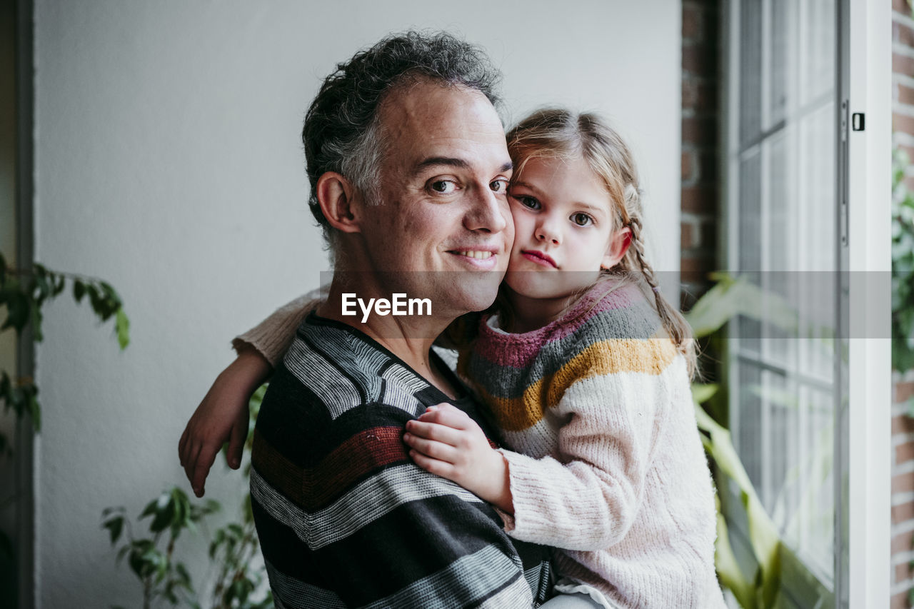 Smiling father carrying daughter while standing by window at home