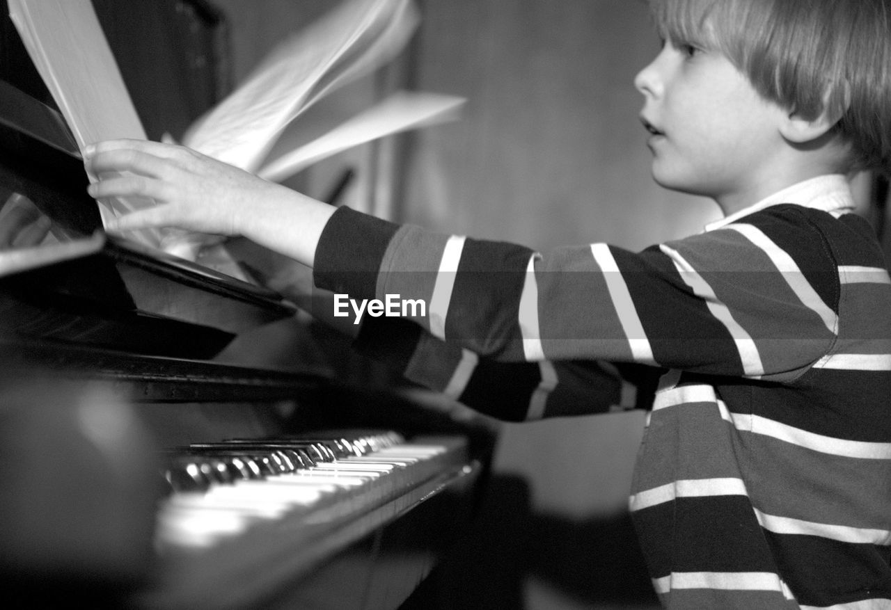 Side view of boy holding sheet music while sitting by piano