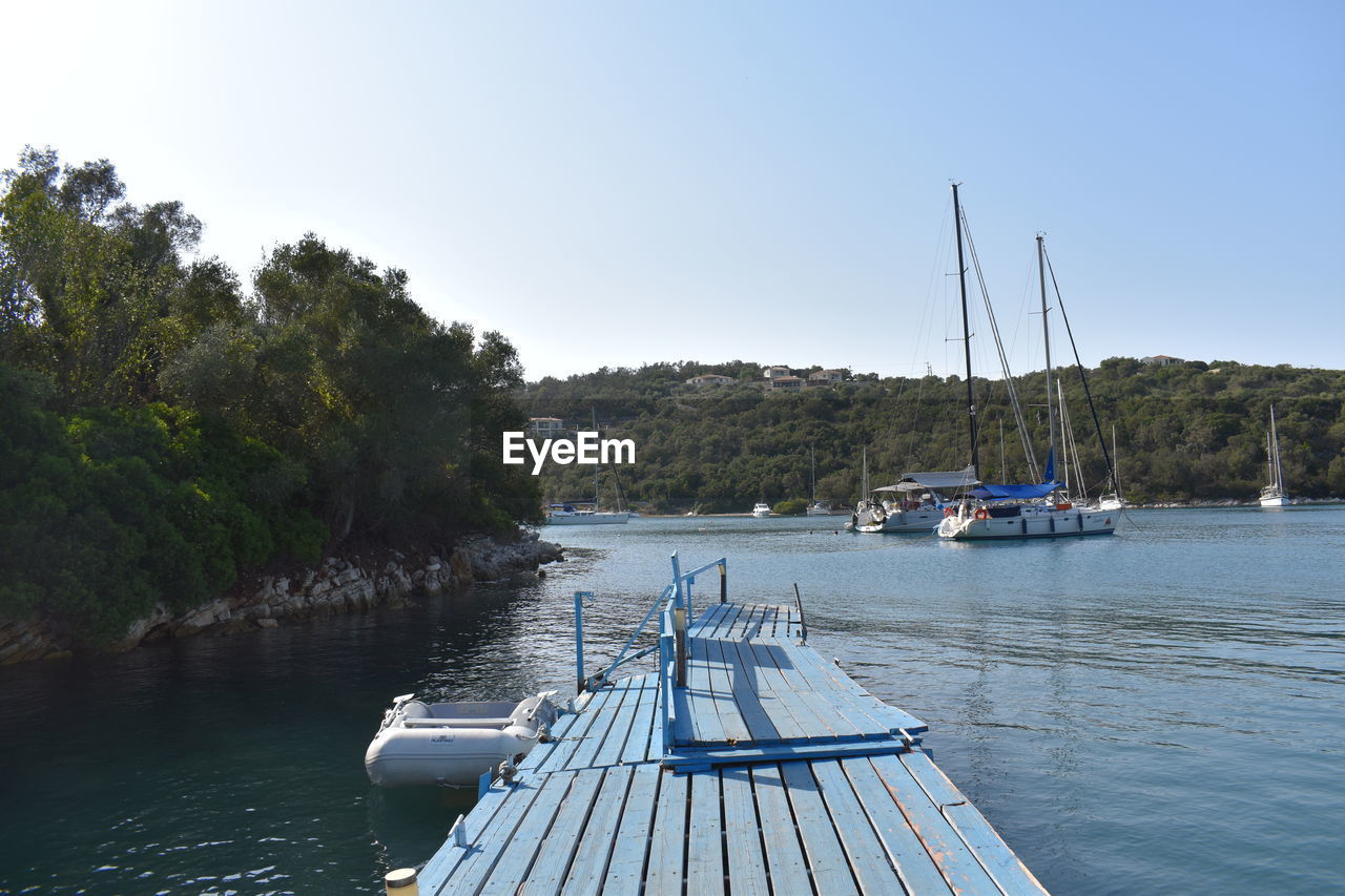 water, nautical vessel, transportation, mode of transportation, nature, sky, sea, boat, vehicle, dock, tree, travel, sailboat, tranquility, beauty in nature, bay, scenics - nature, ship, holiday, clear sky, no people, vacation, travel destinations, plant, tranquil scene, land, trip, pier, marina, day, blue, idyllic, moored, outdoors, beach, tourism, environment, watercraft, summer, sailing, jetty, harbor, landscape, non-urban scene, boating, mast, yacht, wood, sunlight, sunny, architecture, channel, coast, pole, relaxation