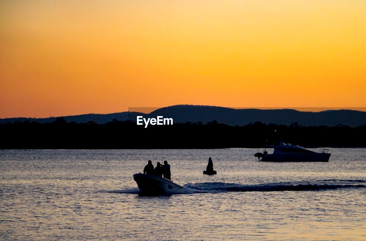 SILHOUETTE BOATS IN SEA AGAINST SUNSET SKY