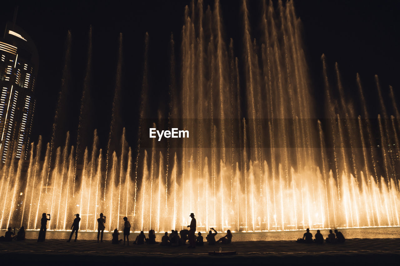 Silhouette people against illuminated fountain at night