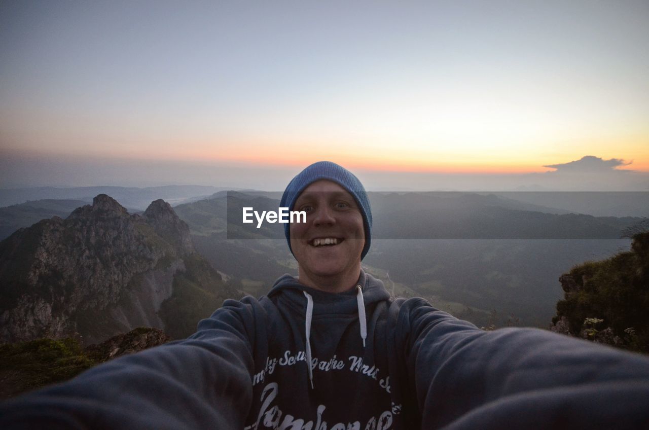 Portrait of cheerful man on mountain against sky during sunset