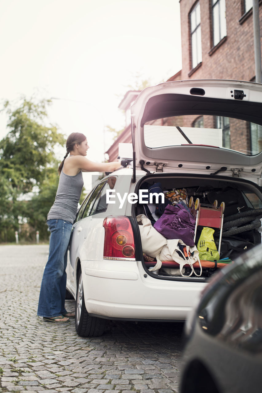 Side view of woman loading luggage on car roof